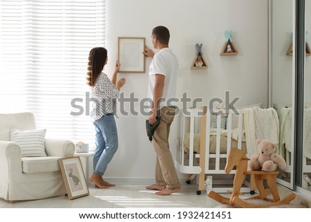 Happy couple decorating baby room with pictures together. Interior design