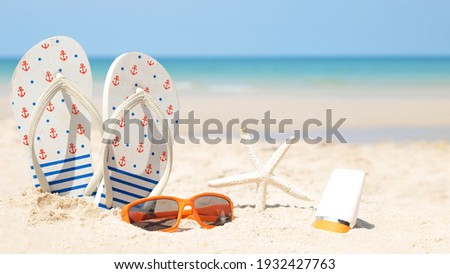 Summer accessories. Planing to travel with sunblock and sandal on the beautiful beach and blue sky background. Tropical fashion. Summer Fashion on holiday concept. 