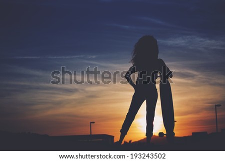 Silhouette of a slender girl with a longboard against the setting sun, hipster colors