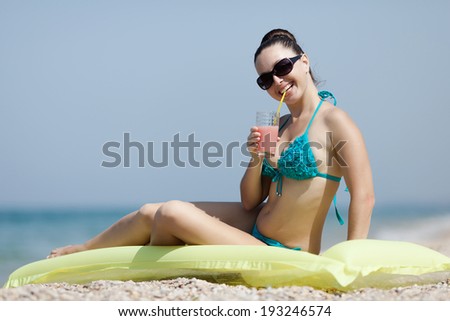 Girl at the sea. Attractive young woman sitting on swimming mattress drinking juice from glass
