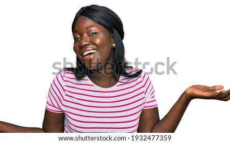 African young woman wearing casual striped t shirt clueless and confused expression with arms and hands raised. doubt concept. 