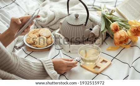 A girl takes pictures on the phone of a spring composition with tea, cookies and tulips in bed. Social media content concept.