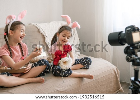 Little sisters with bunny ears pose for the camera with Easter eggs and flowers for decoration. Easter photo session concept.