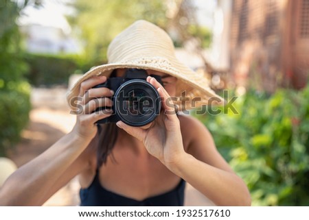 A young woman in a hat takes pictures with a professional SLR camera on a hot summer day.