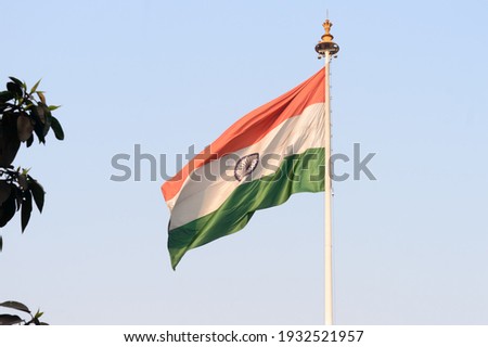 Indian flag flying against blue sky background. The National Flag of India is a horizontal rectangular tricolor (saffron, white and green color) with the Ashoka Chakra at its center.