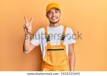 Hispanic young man wearing handyman uniform showing and pointing up with fingers number two while smiling confident and happy. 