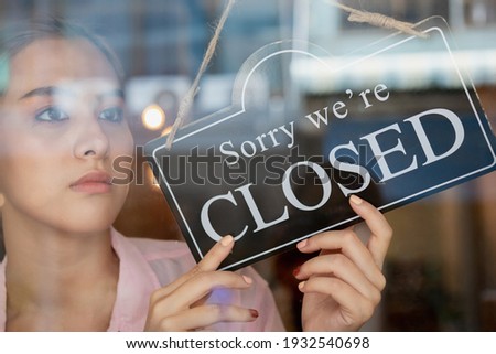 Sad, unhappy young asian owner retail, coffee shop woman turning sign board to closed, protection to pandemic of coronavirus. Close store,restaurant or pub due to lockdown, quarantine of covid.
