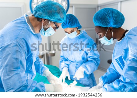 Group of surgeons doing surgery in hospital operating theater. Medical team doing critical operation. Group of surgeons in operating room with surgery equipment. Modern medical background Royalty-Free Stock Photo #1932544256