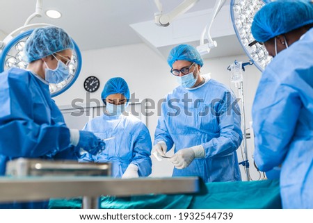 Multi-ethnic healthcare workers performing surgery on patient at operation theater. Medical colleagues operating in emergency room at hospital. They are in scrubs