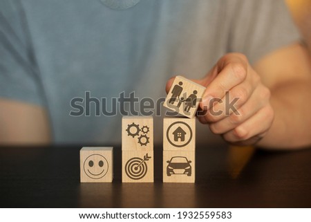 Business and finance concept. Hand holds wooden wooden blocks with finance icons and business. securities, student hat, 
books, time, home, car, family, question, target, gears,  securities, money, id