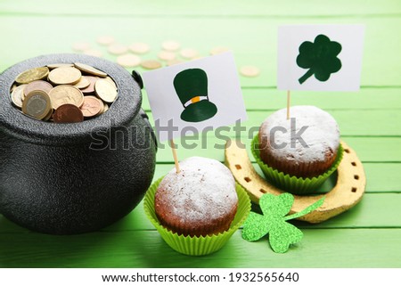 Gold horseshoe with pot of coins, cupcakes, flags with picture of St.Patrick's hat and clover leaf on green wooden background