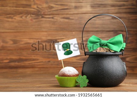 Pot of coins with bow tie, clover leaf, cupcake and flag with picture of St. Patrick's hat on wooden background