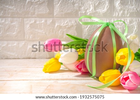 Easter greeting card background with huge big chocolate egg, with festive ribbon tulip flowers bouquet, on sun lighted wooden classic background copy space