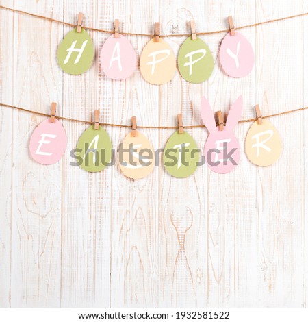 Inscription Happy Easter on colored eggs, on wooden background, a rope with clothespins. The concept of postcards for the Easter holiday.