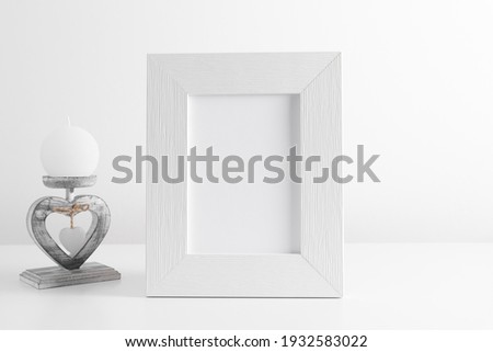 White frame mockup with candle on white table. Front view. Place for text, copy space, mockup