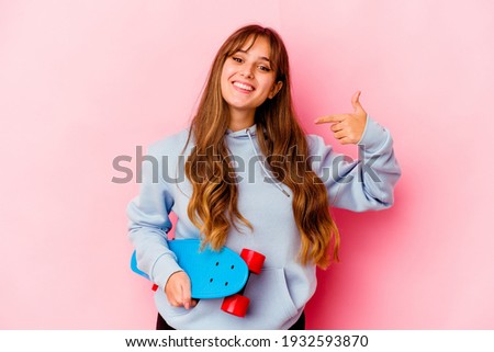 Young skater woman isolated on pink background person pointing by hand to a shirt copy space, proud and confident