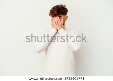 Young Moroccan man isolated on white background blink at the camera through fingers, embarrassed covering face.