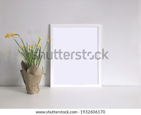 White frame template for a photo or picture in the interior with a bouquet of daffodils