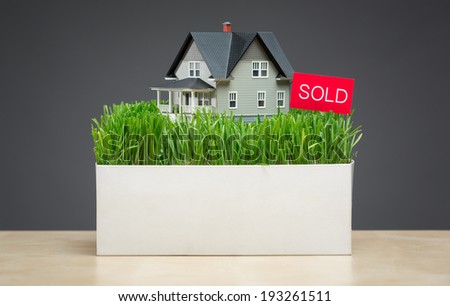 Close up of house model with green grass and sold tablet on grey background. Concept of real estate and sales