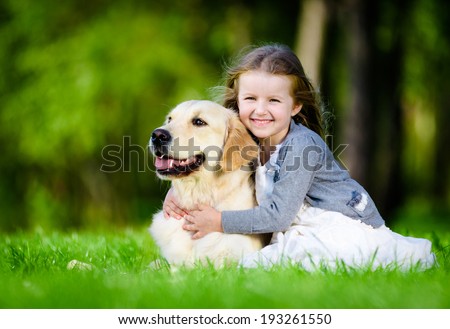 Little girl sitting on the green grass with labrador retriever in the summer park