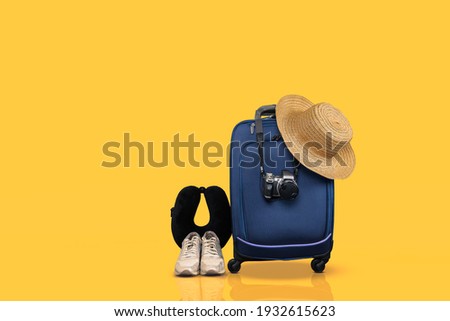 Blue wheeled hand luggage and essential travel items against yellow background.