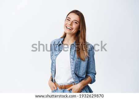 Happy carefree woman with joyful expression, smiling while standing in relaxed pose against white background, holding hands in jeans pockets Royalty-Free Stock Photo #1932629870