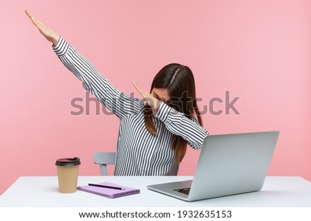 Extremely excited happy woman office worker showing dab dance gesture, performing internet meme of success, sitting at workplace with laptop. Indoor studio shot isolated on pink background Royalty-Free Stock Photo #1932635153