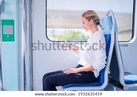 Enjoying travel. Young pretty woman traveling by the metro train sitting near the window using smartphone. Royalty-Free Stock Photo #1932635459