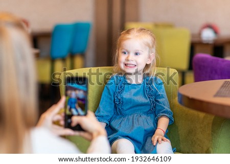 The girl takes a picture of her mother. Child takes pictures of his mother in a cafe