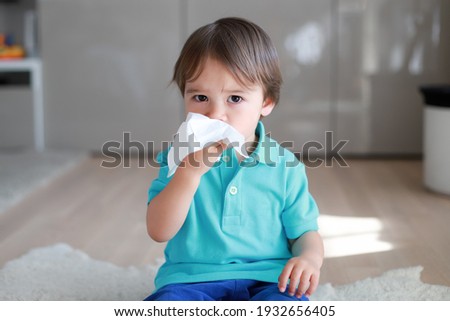 Cute toddler boy blowing nose into tissue paper at home. Mixed race Asian-German baby concept for coronavirus, Covid-19 sickness or allergy. Royalty-Free Stock Photo #1932656405