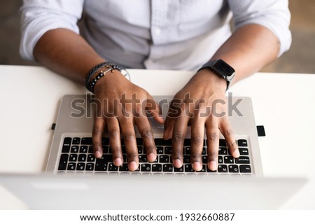 A male hands on the laptop keyboard. Top view an African-American guy is typing email, programmer is develops software, cropped photo, a face is not visible, close-up picture