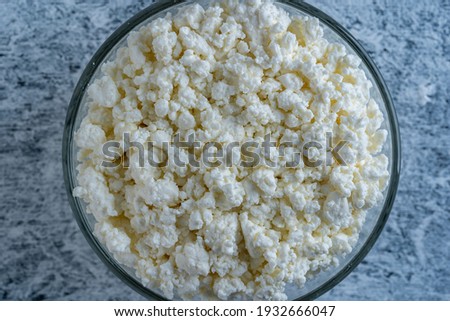Cottage cheese in glass bowl of background, top view. White grainy texture of dairy product, cottage cheese close up. Dairy product concept