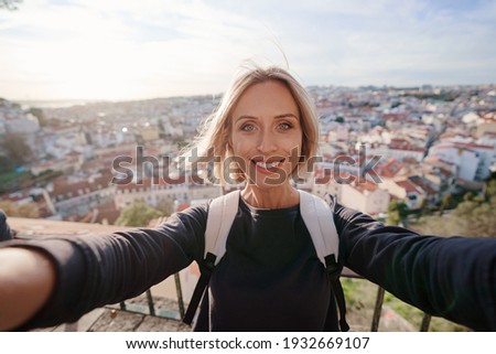 Traveling by Portugal. Young traveling woman taking selfie in old town Lisbon with view on red tiled roofs, ancient architecture.