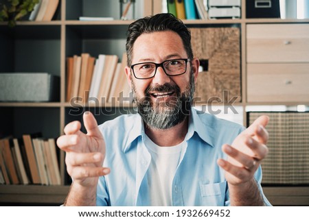 Head shot portrait confident businessman coach wearing glasses looking at camera and talking, mentor speaker holding online lesson, explaining, sitting at wooden work desk in modern cabinet Royalty-Free Stock Photo #1932669452