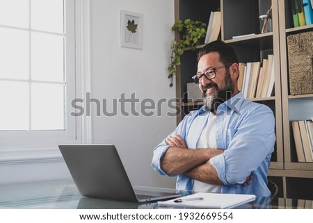 One happy and satisfied man smiling and looking at his job on the computer screen. Male people relaxing after finishing work in the office of home indoor. Royalty-Free Stock Photo #1932669554
