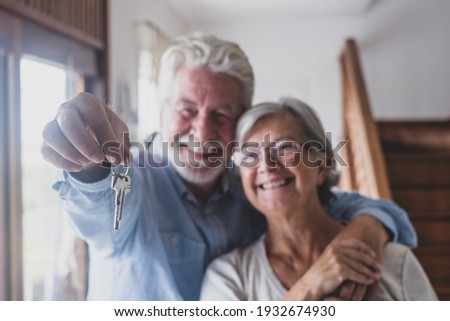 Happy senior old aged woman and man customer landlord hold key to new house apartment give to camera, older retired couple of seniors hand real estate owner make sale purchase property deal concept Royalty-Free Stock Photo #1932674930