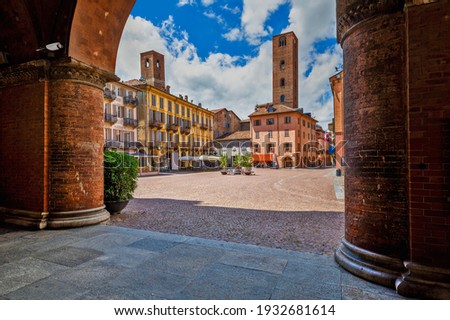 View of cobblestone town square among old houses and medieval towers under beautiful sky in Alba, Piedmont, Northern Italy. Royalty-Free Stock Photo #1932681614