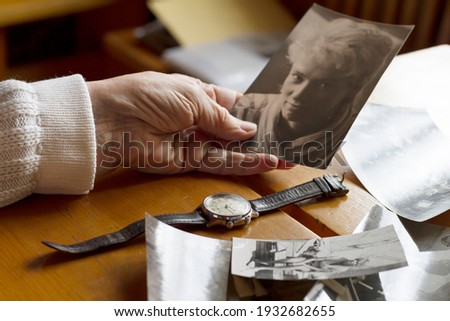 An old watch next to an old woman's hand. Next to old photos. Memories, nostalgia, time concept