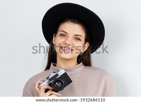 Studio shot of happy girl holding camera. European female model taking photos on white background.