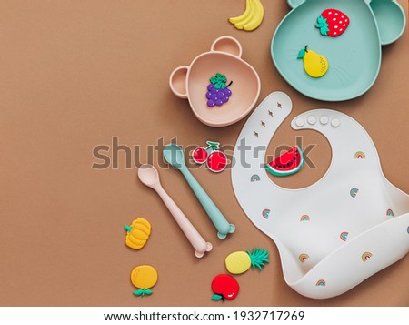 baby dishware on brown background, Flat lay composition with kids accessories, first food for baby, first feeding concept Royalty-Free Stock Photo #1932717269