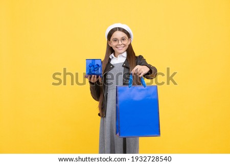 Happy teenage girl back to school holding gift box and paperbag yellow background, shopping bag.