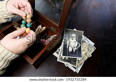 female hands are sorting dear to heart memorabilia in an old wooden box, a stack of retro photos, a wooden rosary, vintage photographs of 1960, concept of family tree, genealogy, childhood memories Royalty-Free Stock Photo #1932735284