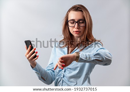 beautiful girl in glasses and a blue shirt looks at the watch on a white background. isolated