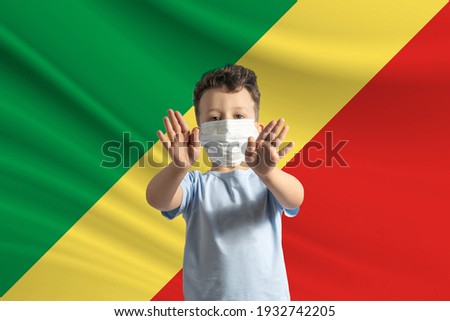 Little white boy in a protective mask on the background of the flag of Republic of the Congo Makes a stop sign with his hands, stay at home Republic of the Congo.