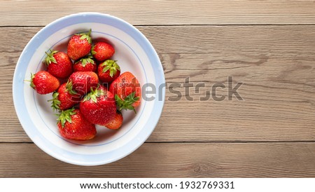 Natural ripe strawberries in a plain white bowl on wooden background. Top view, copy space