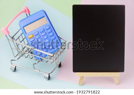 Selective focus of small shopping cart and calculator with chalkboard space for enter text on pastel background. Shopping,check out and payment or expense concept. This photo contains noise and grain.