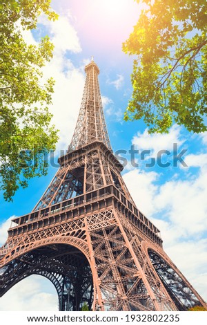 Eiffel Tower against the sky with green trees in Paris, France. Famous travel destination. 