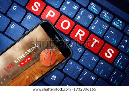 Sports Live streaming concept showing Basketball game broadcast on smartphone with laptop high tech background. Accessible on demand digital content is the future of sports broadcasting.