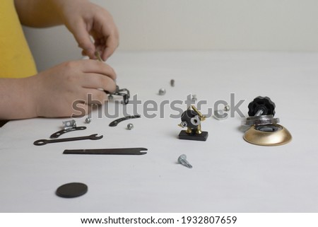 boy in a yellow t-shirt makes robots from metal parts on a white background