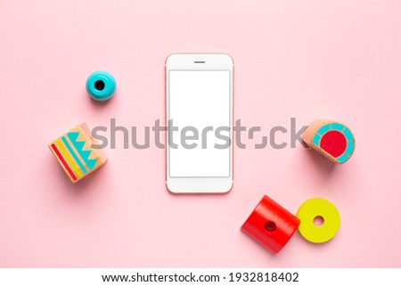 Colorful wooden constructor for children and mobile phone with white screen .Preschool education technology concept with details, screwdriver and screws on pink background top view